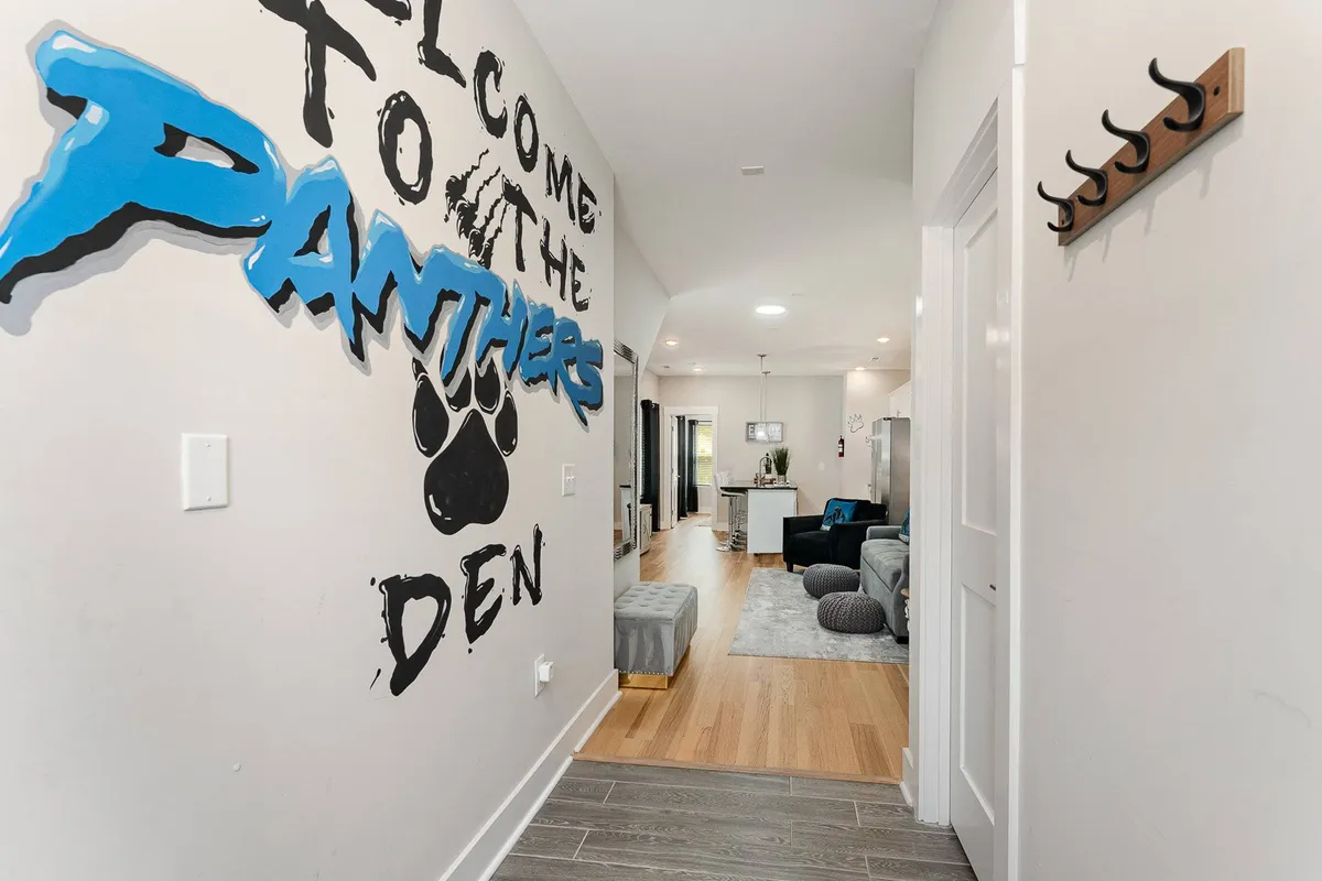 A cheerful entryway with a large mural reading 'Welcome to the Panthers Den', accented by playful paw prints and coat hooks. The space exudes a warm welcome, ideal for greeting guests as they arrive for their group stay.