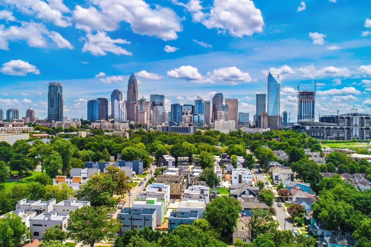 A sweeping view of Charlotte's vibrant downtown skyline, with lush green parks in the foreground and residential areas nestled among the cityscape. The image captures the energetic urban environment and the proximity of community spaces.
