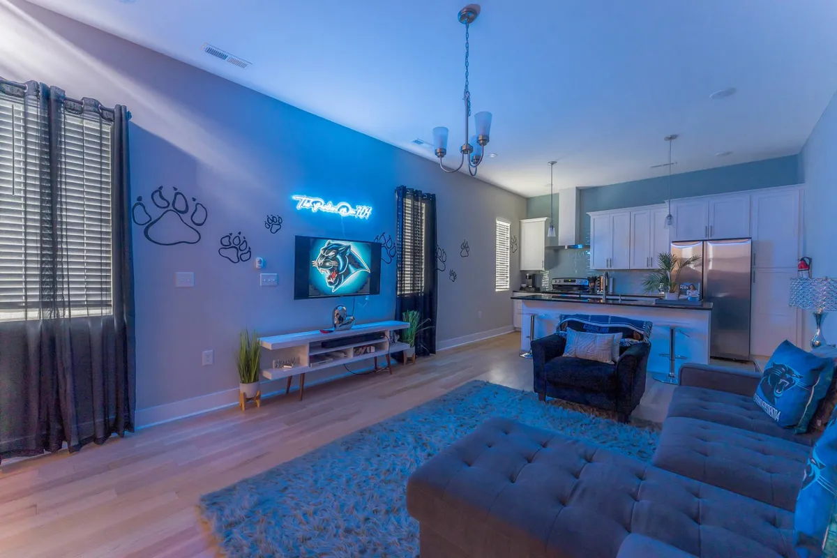 A lively communal living area featuring a plush couch, kitchen area, large artwork, and a neon sign. The room is designed for socializing and relaxation, with ample space for brainstorming sessions or downtime after productive meetings. The playful decor fosters a sense of camaraderie and informal networking among team members.