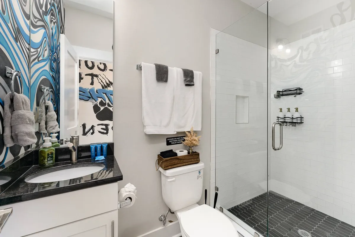 A contemporary bathroom featuring blue abstract wall art, a modern vanity, and a large glass shower. The room is bright and stylish, offering a sense of freshness and comfort.