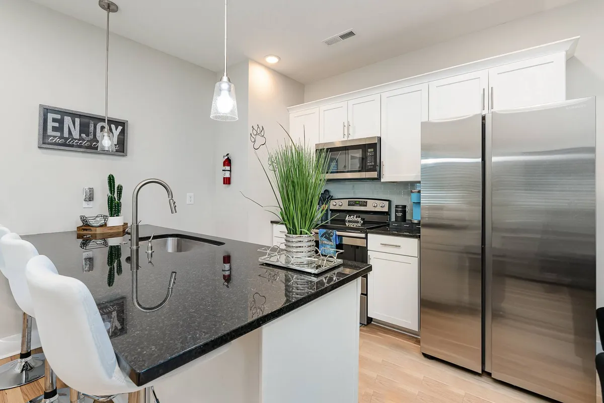 The kitchen is showcased with a welcoming island, stainless steel appliances, bar stools, and a decorative plant. The space looks modern, functional, and perfect for both cooking and socializing.